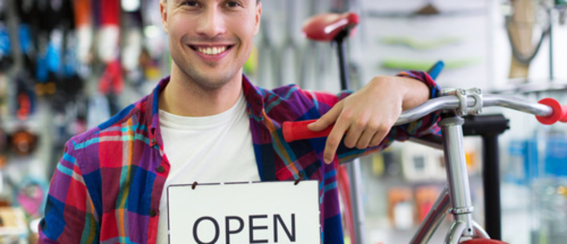 Man in bike shop holding open sign