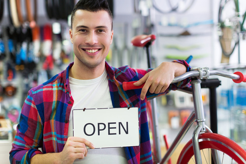 Man in bike shop holding open sign